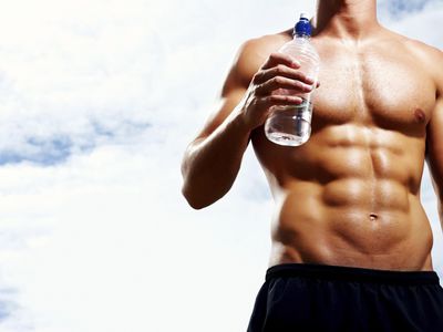 Mid section of muscular man with bottle aganist cloudy sky