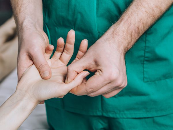 A male massage therapist puts pressure on a sensitive point on a woman's hand.