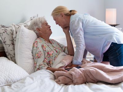 A senior woman in her bed embracing her daughter with emotion