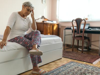 A person sitting on bed with hand to head