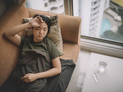 an asian chinese young female lying on sofa with sickness cover with blanket