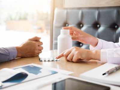 Close-Up Of Doctor Explaining Medicines To Patient At Desk In Hospital