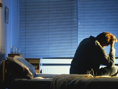 Distressed looking man sitting on hospital bed, head in hand, night