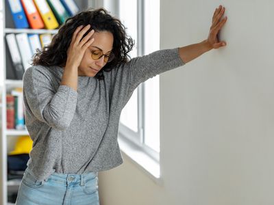 A person feels dizzy and is leaning against a wall indoors