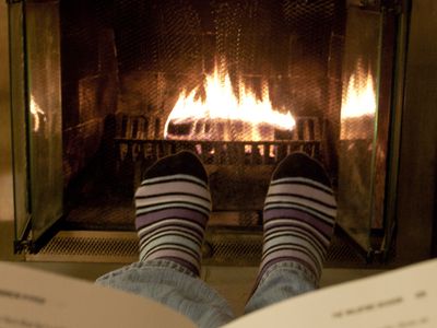 Feet in socks being warmed by a fire in a brick fireplace.