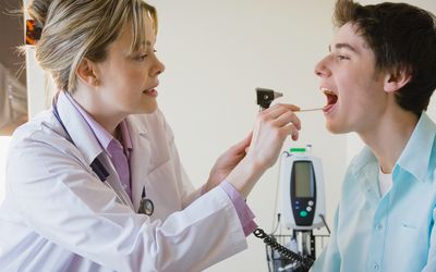 Female doctor checking teen patient's throat 