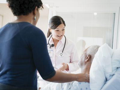 Female doctor talking with senior patient lying by daughter in hospital ward