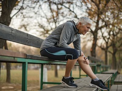 Woman appearing in pain sitting on a bench holding her leg