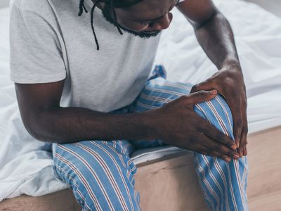 A man sits on a bed, holding his knee