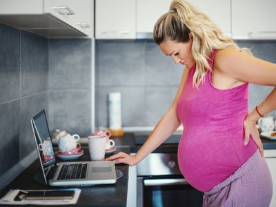 Pregnant woman standing with hand on back 