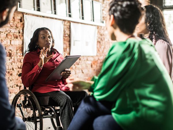 A group of people sitting and facing a person in wheelchair who is leading a work meeting