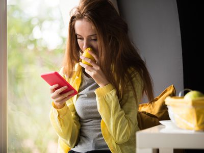 Shot of happy young woman smelling a lemon while relaxing on the window sill and scrolling through social media on her smart phone.