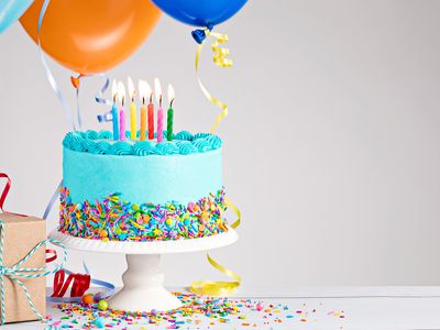 Blue-frosted birthday cake with balloons, a package, and a birthday hat