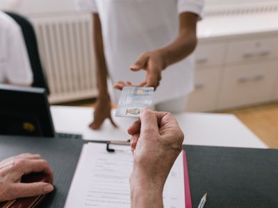 Woman Handing Receptionist Medical Insurance Card At MRI Clinic Reception