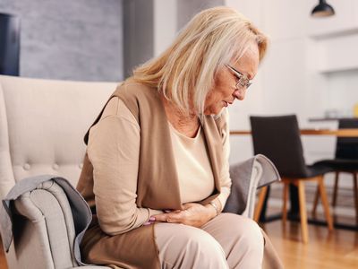 Person experiencing digestive distress at home. She is seated and bent forward with her hands near her stomach and cramps.