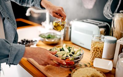 Person pouring olive oil on salad