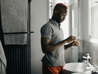 Man standing in a bathroom, looking at a COVID test swab