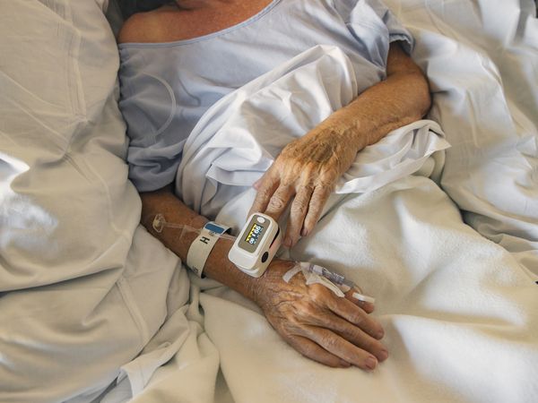 Unrecognizable older adult lying in a hospital bed with pulse oximeter on their finger and IV in their arm