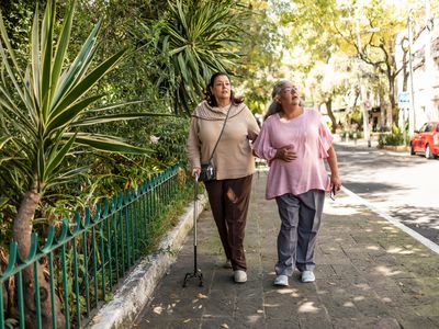 Woman with multiple sclerosis uses cane while walking with a friend