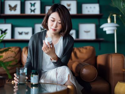 Young woman sitting on a sofa at home, reading the label of a medication or supplement