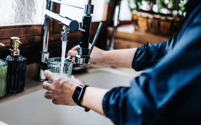 Close up of man wearing a watch filling a glass with tap water. 