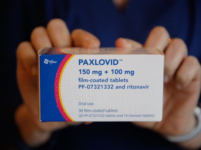 A box of PAXLOVID being help up by an unseen person.