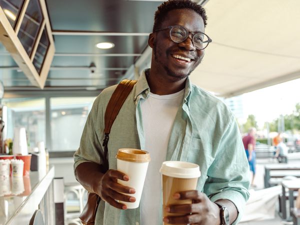 Portrait of a man wearing glasses, smiling while holding two cups of coffee