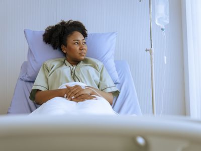 Young woman hooked up to an IV sitting in a hospital l bed looking out the window