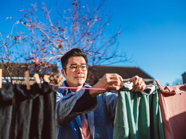 Young man hanging laundry on a clothesline on a sunny day with the blue sky above him. 