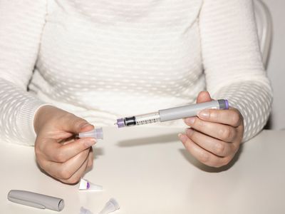 Unseen person in a white sweater holding an autoinjector pen