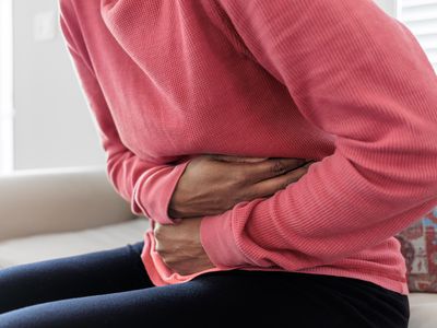 A woman sitting on the couch holding her abdomen in pain