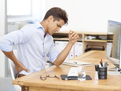 a man holding his back sitting at a desk