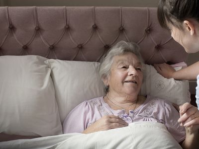 A personal care assistant chatting with a senior woman who is in bed