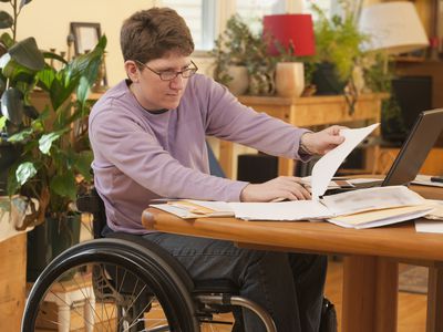 Young person with MS who uses a wheelchair, doing paperwork at home