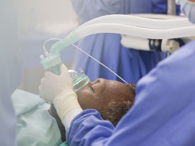 Close up of doctor wearing surgical gloves, holding oxygen mask over patient in operating theater