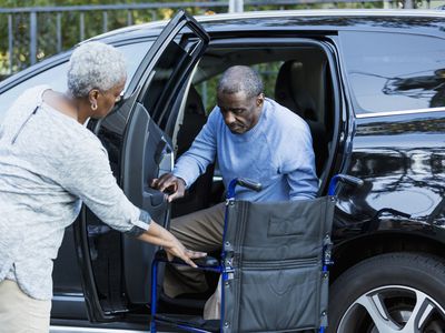 A family caregiver helps a person with multiple sclerosis get out of vehicle and into wheelchair