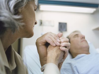 Old man in hospital bed holding hands with woman