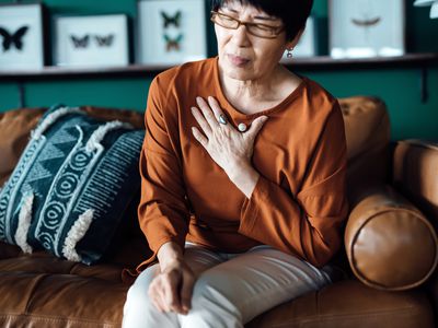 A person sitting at home on the couch experiencing chest discomfort that may signal a heart attack