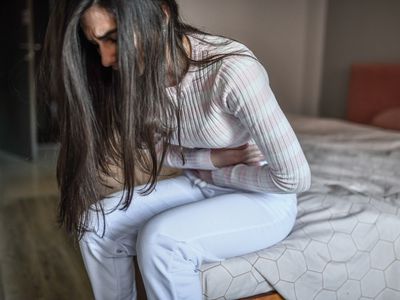 A person has abdominal pain from IBS while sitting on a bed