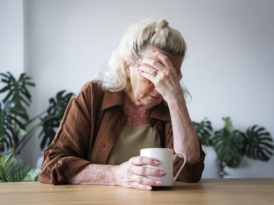 A person with MS feels fatigue, holding mug with hand on forehead