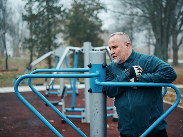 An older adult feeling chest pain outdoors at an exercise station