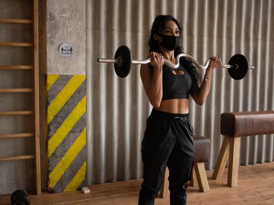 A Black woman wearing a face mask lifting weights.