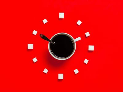 Cup of black coffee with a spoon surrounded by white sugar cubes on a bright red background