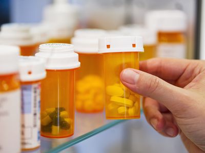 a hand picking up pill bottles on shelf