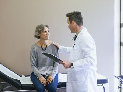 Smiling patient talking with doctor while sitting on bed at hospital