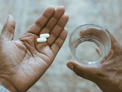 Person holding two pills and a glass of water.