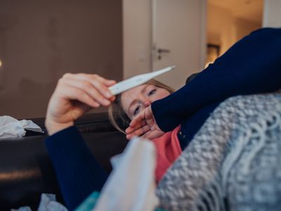 woman under blanket looking at thermometer