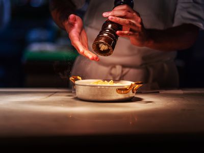 Person grinding black pepper over pasta dish