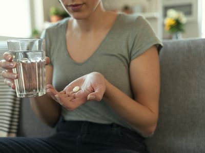 Women holding a pill in her hand with a glass of water