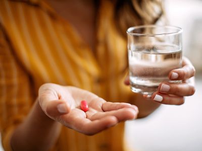 Adult female holding a supplement pill and glass of water in hand